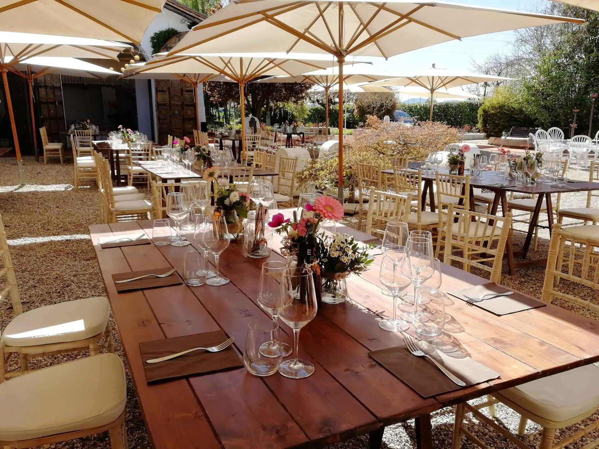 Allestimento all’aperto con tavoli in legno, fiori freschi e calici per evento estivo